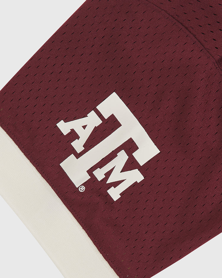 A close-up of the Texas A&M Mesh Football Jersey by Ebbets Field reveals maroon athletic fabric with perforations, a bold white ATM logo, and a crisp white band at the bottom—classic vintage-inspired details reminiscent of traditional Texas A&M football jerseys.