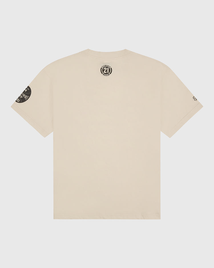 Beige short-sleeve t-shirt from Ebbets Field shown from the back, featuring a circular black 21 graphic near the neck and an additional black graphic on the left sleeve. The Clemente Museum x Ebbets Field Short Sleeve Graphic T-Shirt is a subtle tribute to Roberto Clemente—perfect for celebrating Roberto Clemente Day or showing your appreciation with this classic Clemente-inspired tee.