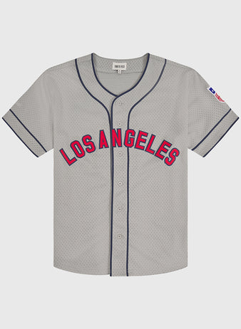 The Ebbets Field Los Angeles Angels (PCL) 1942 Mesh Button-Up Road Jersey features a gray design with “Los Angeles” in red and blue lettering on the front, blue piping, a button-up front, and a small American flag patch on the left sleeve.