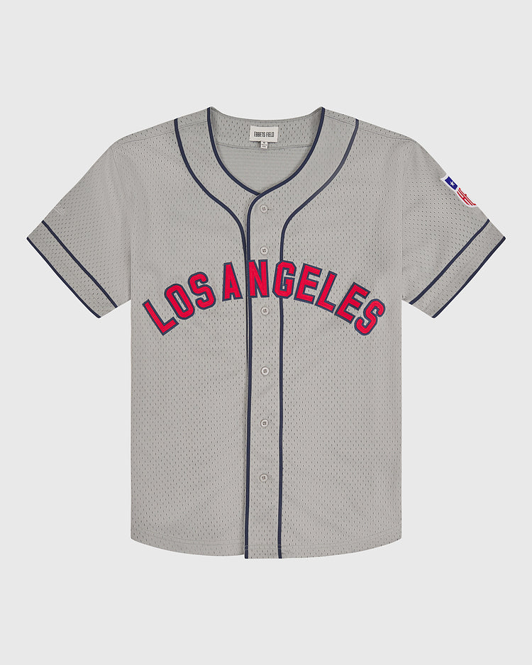 The Ebbets Field Los Angeles Angels (PCL) 1942 Mesh Button-Up Road Jersey features a gray design with “Los Angeles” in red and blue lettering on the front, blue piping, a button-up front, and a small American flag patch on the left sleeve.