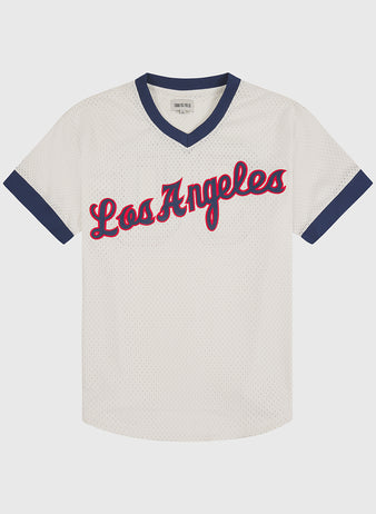 White mesh Los Angeles Angels (PCL) 1957 V-neck home jersey by Ebbets Field, featuring a navy blue V-neck collar and sleeve trim, with “Los Angeles” in red cursive script outlined in navy. Ebbets Field brand label on hem.