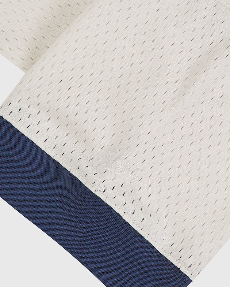 Close-up of an off-white mesh fabric garment with tiny holes and a navy blue ribbed cuff. The brand Ebbets Field is embroidered in white near the cuff on the Los Angeles Angels (PCL) 1957 Mesh V-Neck Home Jersey.
