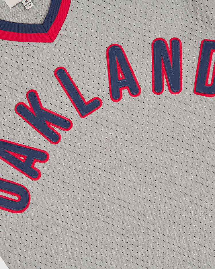 Ebbets Field Oakland Oaks 1948 V-Neck Mesh Road Jersey in gray mesh features red and blue trim around the collar and bold “OAKLAND” lettering in large red letters outlined in blue across the chest.