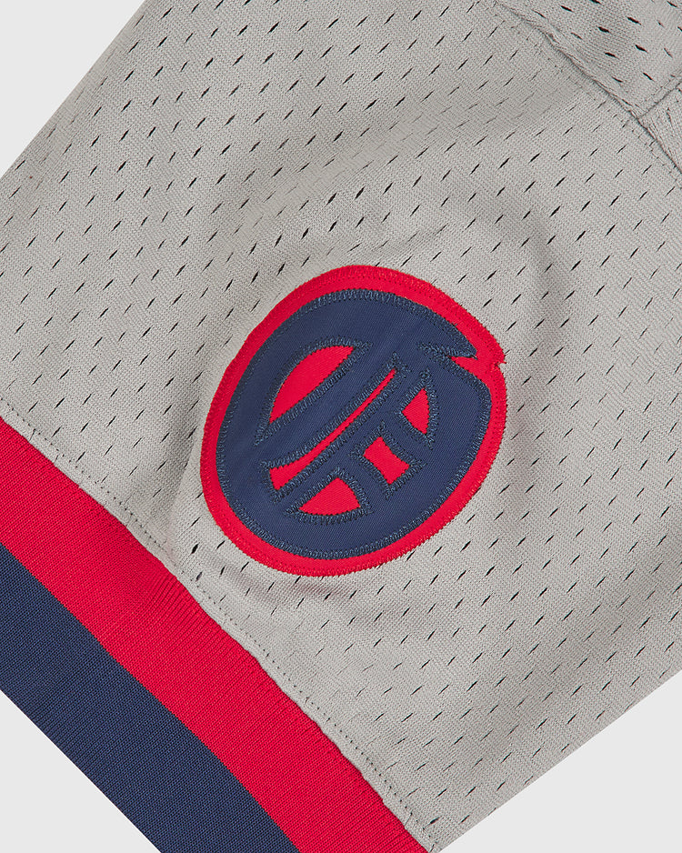 A close-up of the Ebbets Field Oakland Oaks 1948 Mesh V-Neck Road Jersey highlights the gray mesh athletic fabric, accented by a blue and red circular “EH” logo and finished with a red and navy blue striped hem at the bottom.