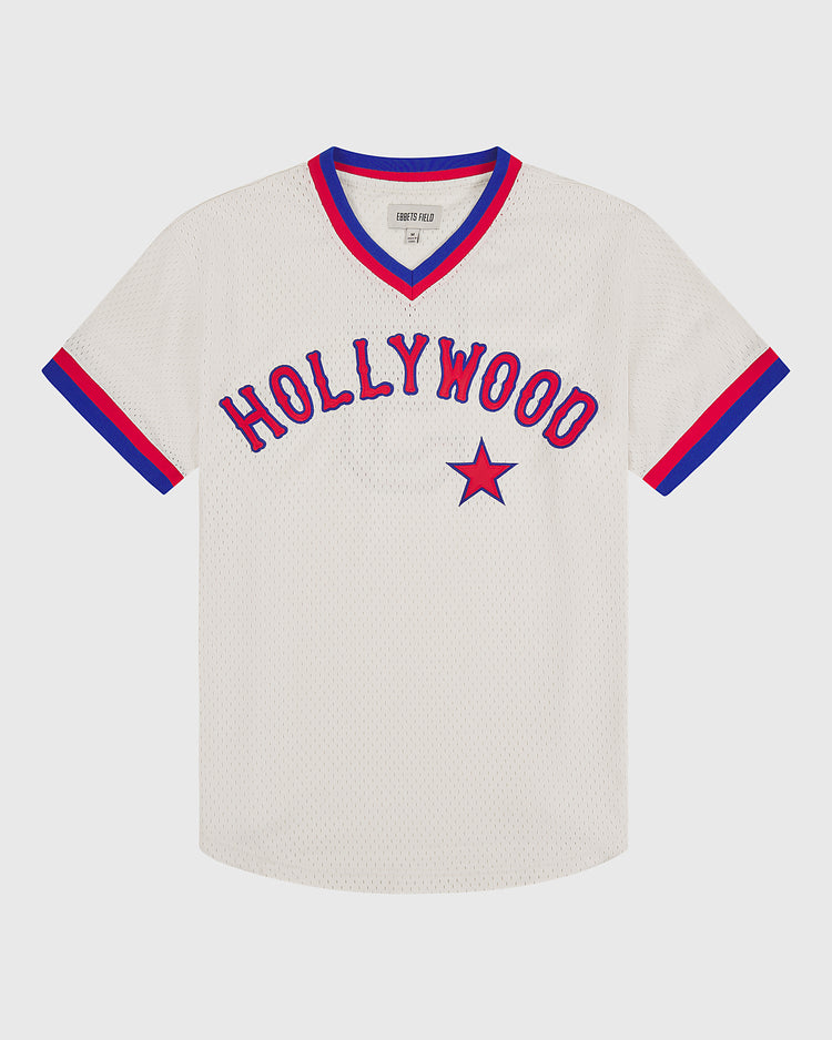 The Hollywood Stars 1940 Mesh V-Neck Home Jersey by Ebbets Field features a white short-sleeve design with “HOLLYWOOD” in bold red letters and a red star underneath. Blue and red trim accents the V-neck collar and sleeve cuffs.