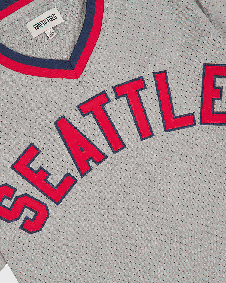 A gray Seattle Rainiers 1951 Mesh V-Neck Road Jersey by Ebbets Field, featuring red and navy trim and large red outlined letters spelling “SEATTLE” across the chest. A white tag inside the collar displays the Ebbets Field brand.
