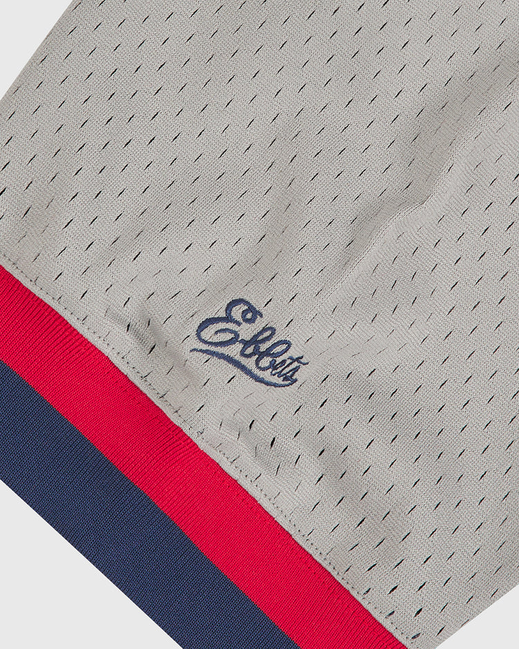 Close-up of light gray mesh fabric with small holes, featuring navy blue “Ebbets Field” script embroidery and red and navy blue stripes on the hem, from the Seattle Rainiers 1951 Mesh V-Neck Road Jersey.