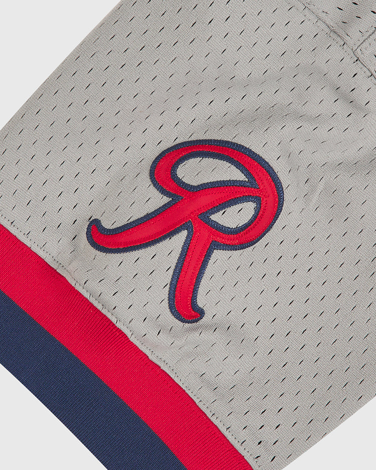 Crafted by Ebbets Field, the Seattle Rainiers 1951 Mesh V-Neck Road Jersey features gray mesh fabric accented with a red and blue ‘R’ patch, finished off with a bold red stripe and a slimmer navy blue stripe along the edge.