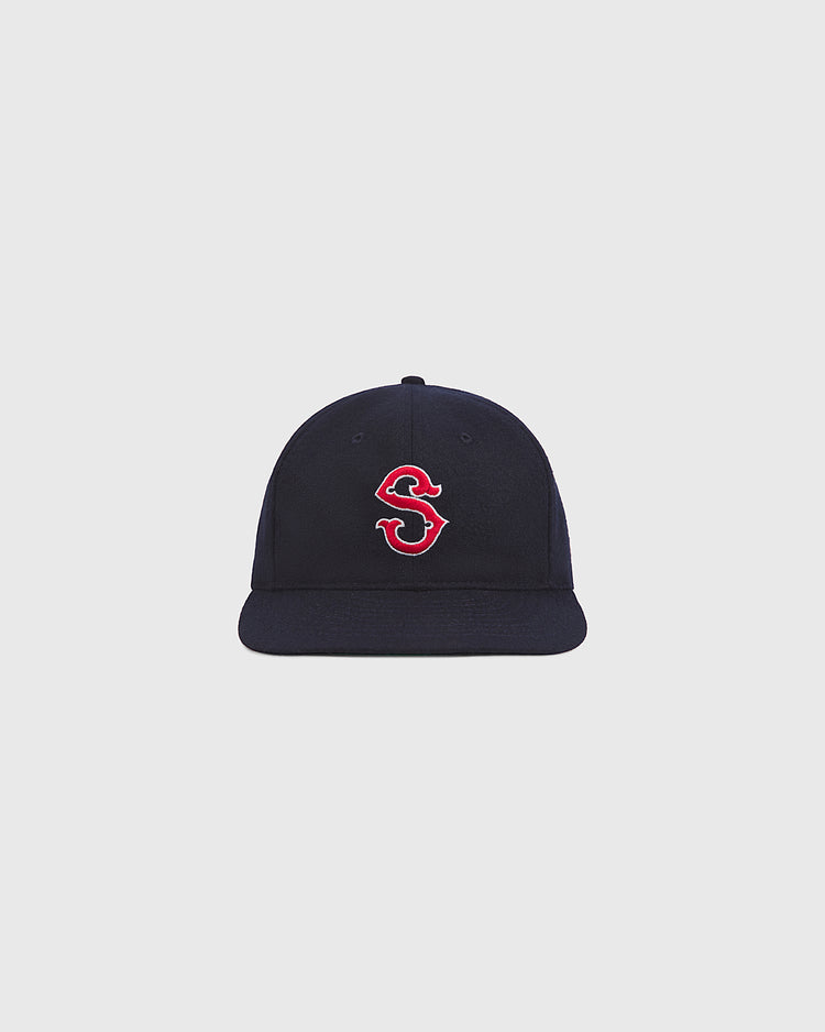 An authentic Seattle Rainiers 1950 wool ballcap by Ebbets Field, featuring a navy blue design and a red and white embroidered “S” on the front, is displayed against a plain light gray background.