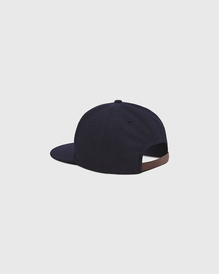 The Seattle Rainiers 1950 Authentic Wool Ballcap by Ebbets Field is shown from the back, featuring an adjustable brown strap with a metal clasp. This dark blue vintage hat has a simple design with minimal visible details and is set against a plain light gray background.