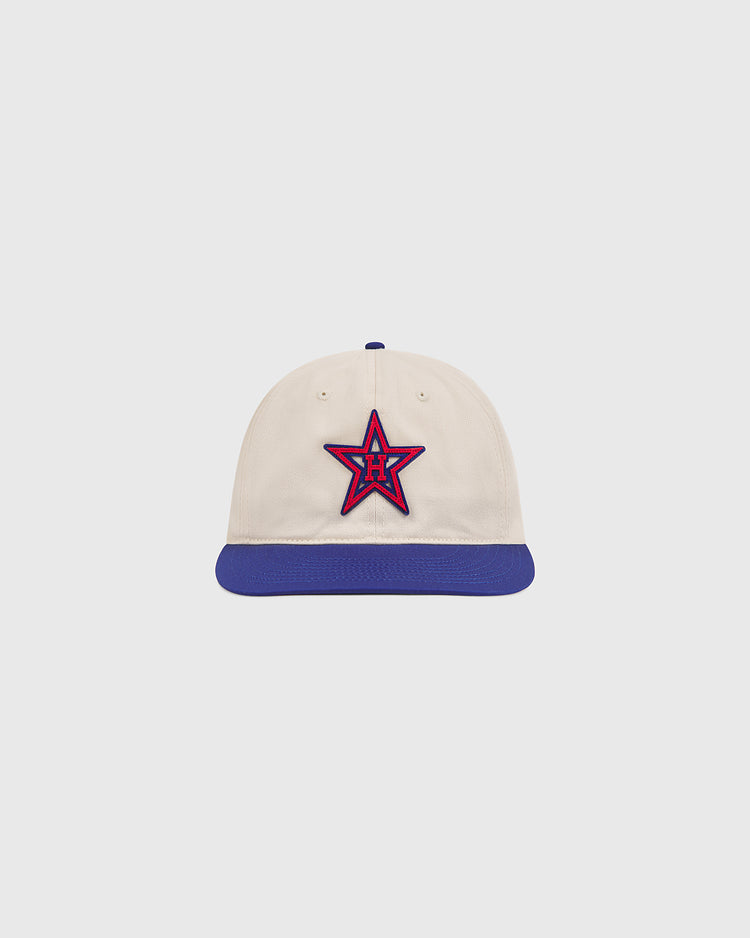 The Ebbets Field Hollywood Stars 1957 Cotton Twill Ballcap, inspired by the 1957 Hollywood Stars and reminiscent of games at Gilmore Field, features a cream-colored cotton twill crown, a blue brim, and a red and blue star emblem with the letter H on the front, displayed on a plain light background.