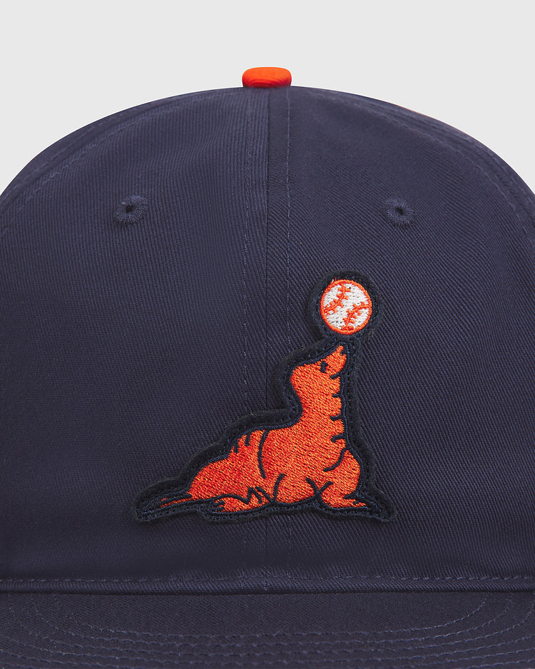 The Ebbets Field San Francisco Seals Cotton Twill Ballcap is a classic navy blue baseball hat featuring an embroidered orange seal balancing a baseball on its nose, inspired by vintage styles and reminiscent of the iconic San Francisco Seals ballcap.