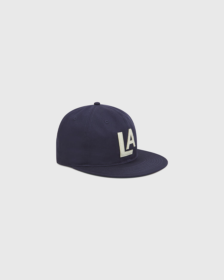 The Ebbets Field Los Angeles Angels (PCL) 1942 Cotton Twill Ballcap features a navy blue design with a flat brim and bold white LA lettering on the front, inspired by the original 1942 baseball hat, shown against a plain light gray background.