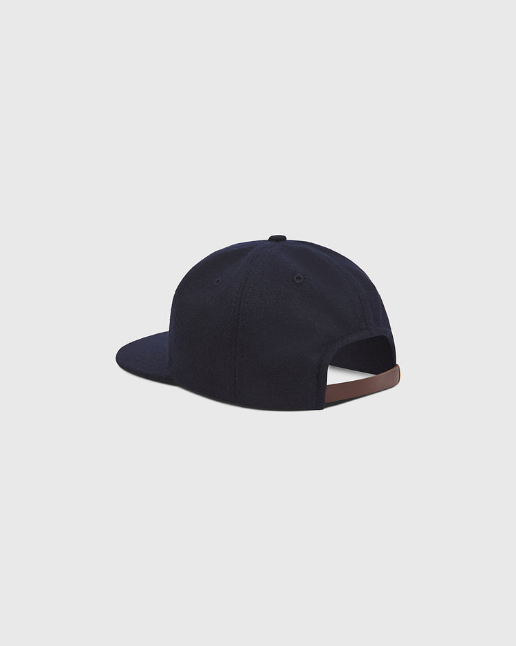 The Ebbets Field San Francisco Seals 1957 Authentic Wool Ballcap, styled as a vintage baseball hat in dark blue wool, is displayed from the back with a brown adjustable strap and a closed opening above it, set against a plain light grey background.