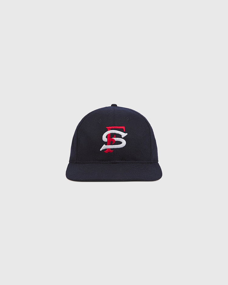 The Ebbets Field San Francisco Seals 1957 Authentic Wool Ballcap features a navy blue wool construction with a red and white embroidered “S and B” logo on the front, inspired by a vintage 1957 baseball hat, and is displayed against a plain light gray background.