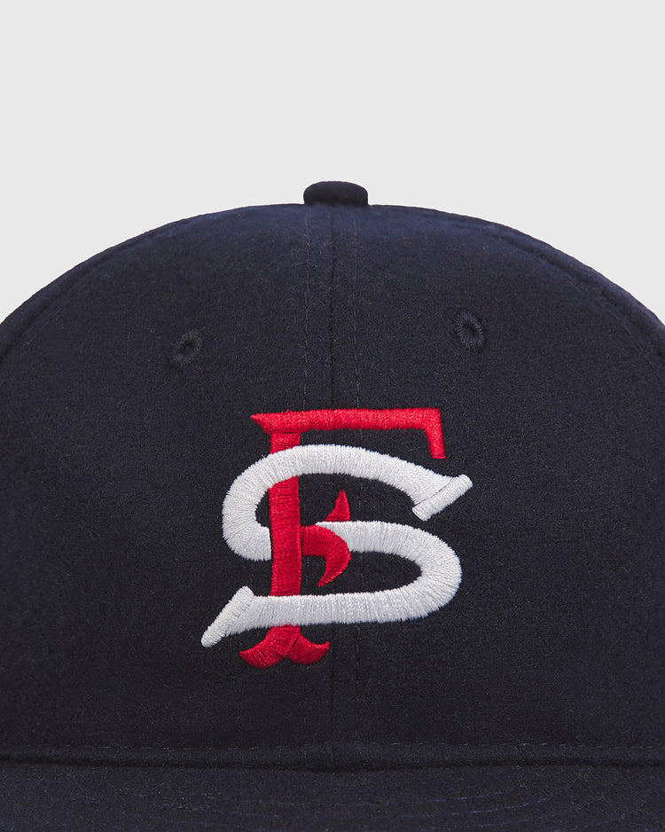 The Ebbets Field San Francisco Seals 1957 Authentic Wool Ballcap is a vintage-style navy blue hat, featuring an embroidered intertwined red and white FS logo on the front, reminiscent of those worn by the Seals in 1957. Displayed against a plain light gray background.
