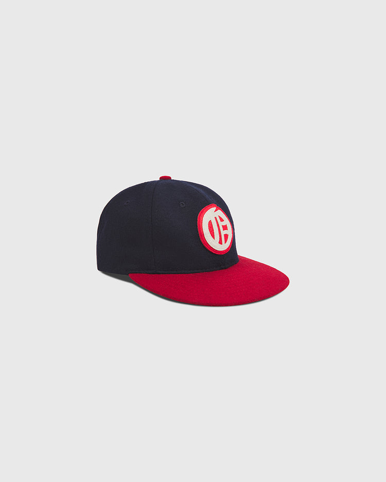 The Ebbets Field Oakland Oaks 1948 Authentic Wool Ballcap is a vintage-inspired navy blue baseball hat with a bold red brim and a distinctive white and red circular logo on the front, shown against a plain light gray background.