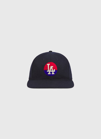 The Ebbets Field Los Angeles Angels (PCL) 1946 Authentic Wool Ballcap is a navy blue cap with a flat brim. The front displays a circular red and blue patch featuring white “LA” lettering at the center, inspired by the iconic 1946 Los Angeles Angels of the Pacific Coast League. The background is plain and light gray.