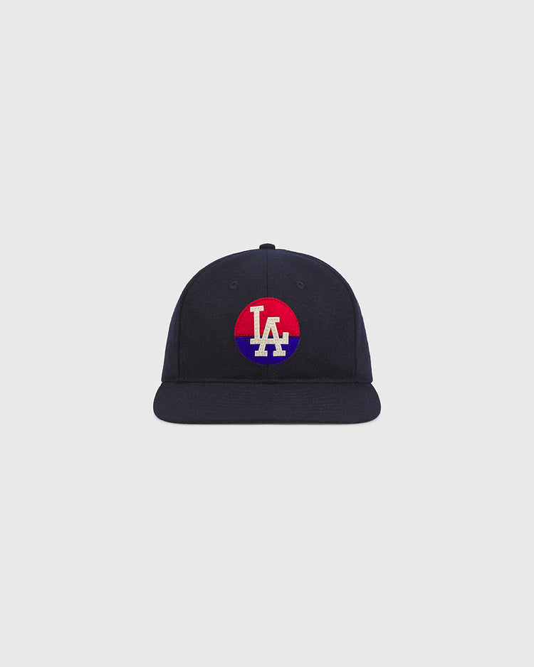 The Ebbets Field Los Angeles Angels (PCL) 1946 Authentic Wool Ballcap is a navy blue cap with a flat brim. The front displays a circular red and blue patch featuring white “LA” lettering at the center, inspired by the iconic 1946 Los Angeles Angels of the Pacific Coast League. The background is plain and light gray.