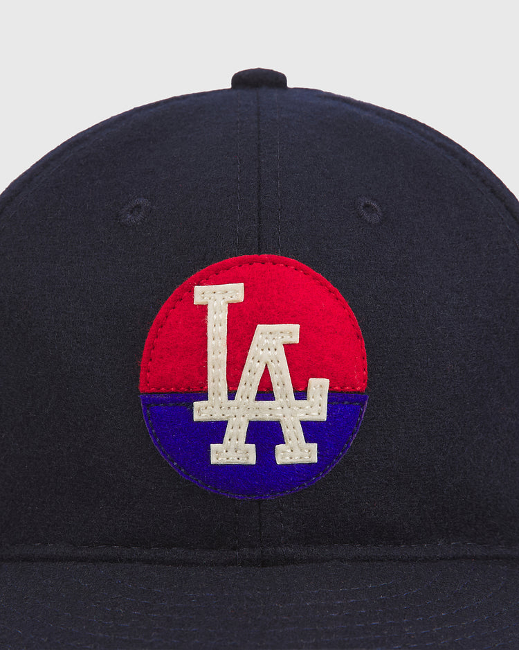 The Ebbets Field Los Angeles Angels (PCL) 1946 Authentic Wool Ballcap is a navy blue cap with a red and blue circle featuring white embroidered “LA” letters in the center, inspired by the classic 1946 Pacific Coast League team.