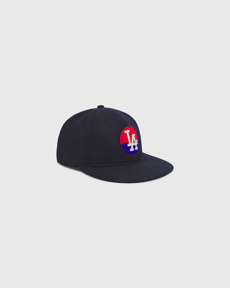 The Ebbets Field Los Angeles Angels (PCL) 1946 Authentic Wool Ballcap, crafted in navy blue wool and adorned with a red, white, and blue circular patch featuring the white “LA” letters on the front—reminiscent of the 1946 Pacific Coast League team—is displayed on a plain gray background.