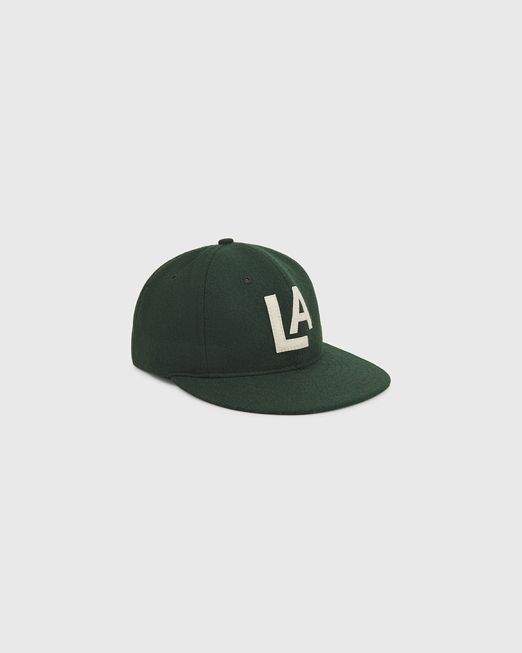 The Los Angeles Angels (PCL) 1942 Authentic Wool Ballcap by Ebbets Field is a dark green, flat-brimmed cap featuring prominent white “LA” lettering on the front, modeled after the historic 1942 Los Angeles Angels Pacific Coast League design and shown against a plain light gray background.