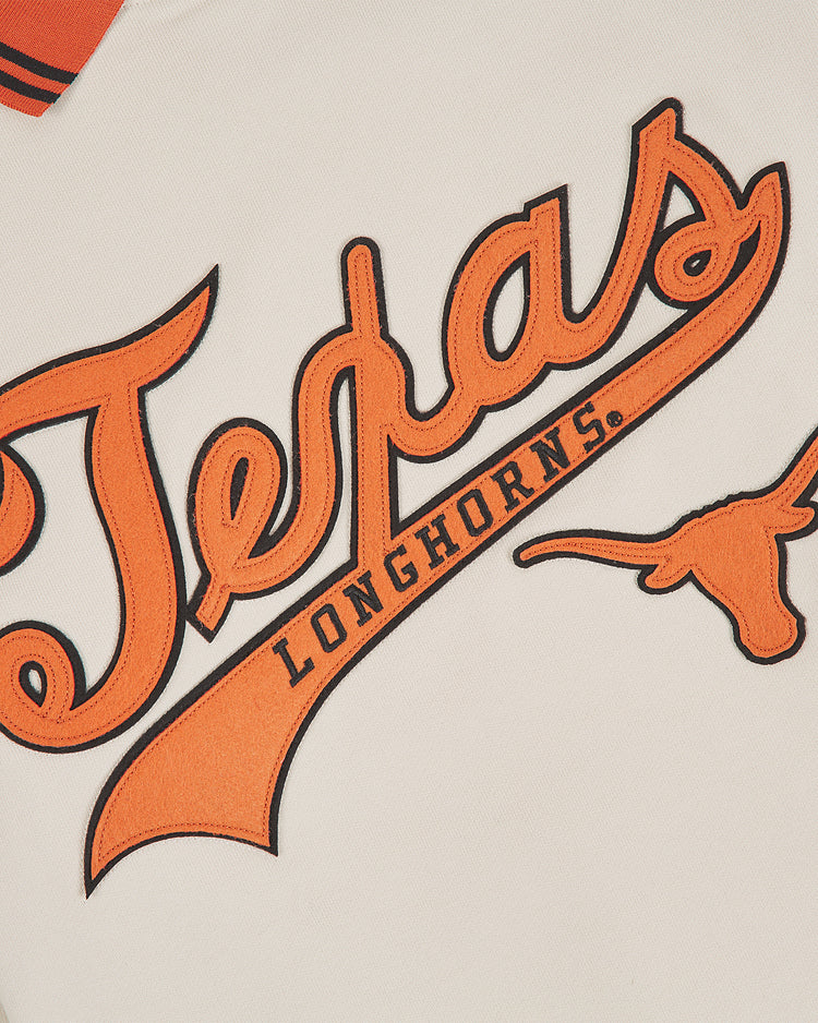 Close-up of “Texas Longhorns” embroidered in orange and black script on the white fabric of the Ebbets Field University of Texas Collared Crewneck, with a Longhorn steer head logo to the right of the text.