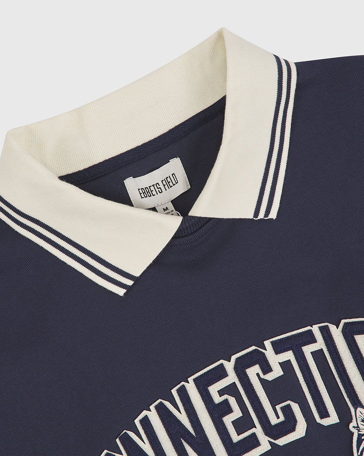 University of Connecticut Collared Crewneck by Ebbets Field, featuring a navy body with white collar and navy stripes, CONNECTICUT in bold white letters on the front, and an Ebbets Field label sewn inside the neckline.