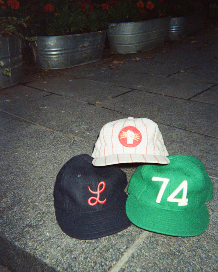 Three Ebbets Field Mystery Caps of Mexico – 74 Regimento de Puebla 1925 Wool Ballcaps: a navy blue with a red script L, a green with white 74, and a cream pinstriped one with a red circular emblem featuring a clenched fist.