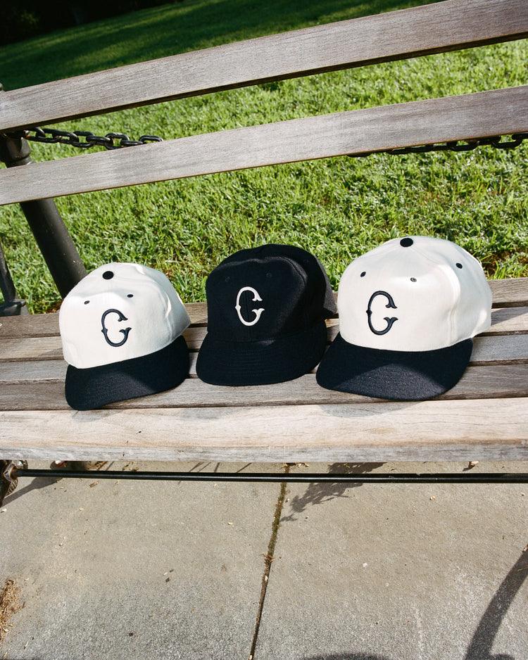 Three baseball caps, including the EFF University of Connecticut 1957 Vintage Ballcap, are displayed on a wooden bench outdoors with green grass in the background.