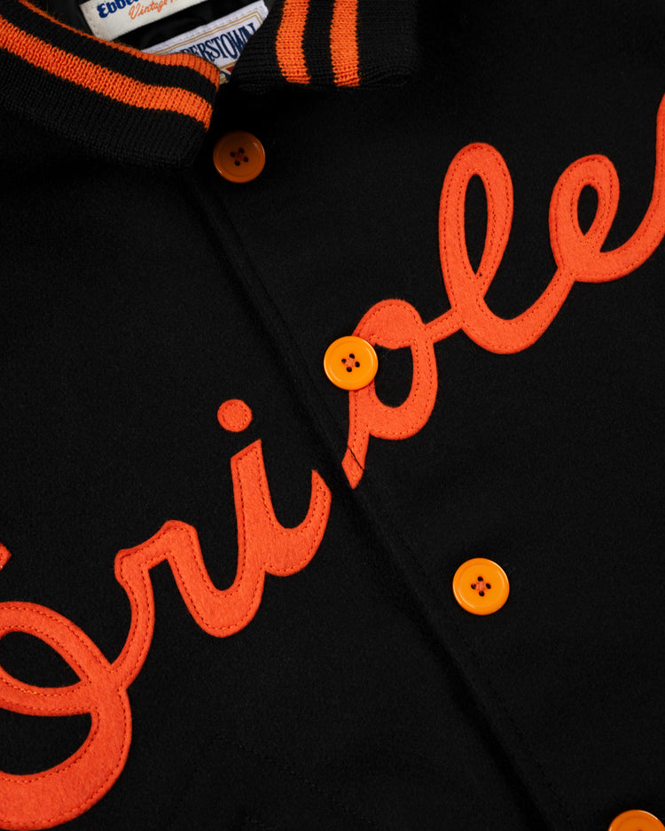 Close-up of a black EFF Baltimore Orioles 1966 Authentic All Wool Varsity Jacket featuring bright orange buttons and Orioles script, inspired by the teams 1966 design. A label is partially visible inside the collar.