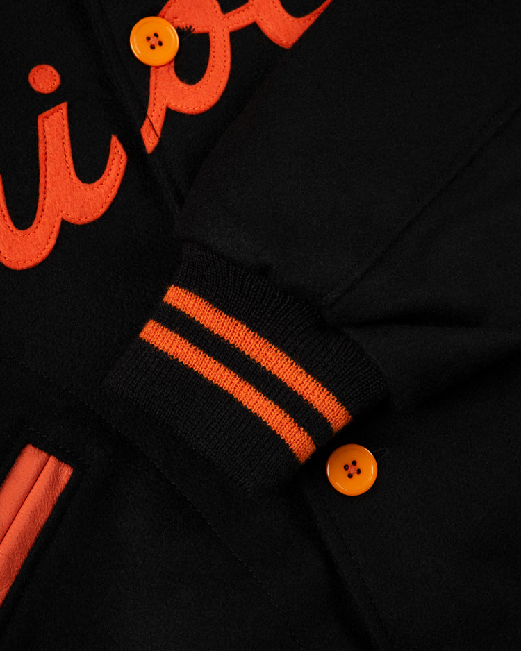 Close-up of the EFF Baltimore Orioles 1966 Authentic All Wool Varsity Jacket, showcasing orange buttons, an embroidered letter, orange and black striped ribbed cuff, and an orange-trimmed pocket.
