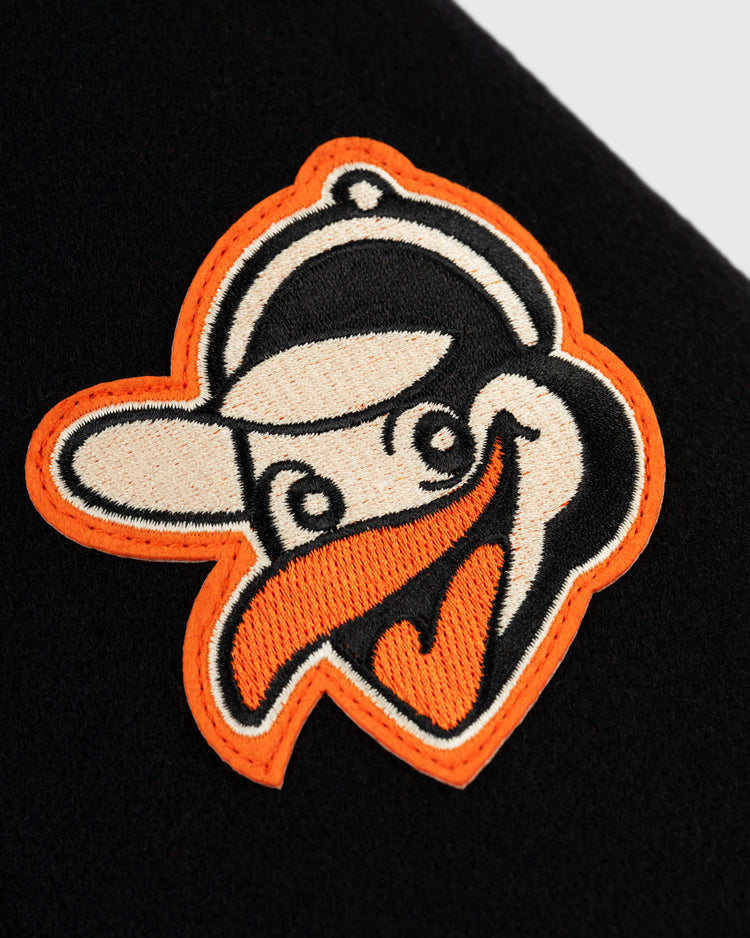 Close-up of a stitched cartoon bird head with a baseball cap, outlined in orange, white, and black, on black fabric—mirroring the iconic detail from the EFF Baltimore Orioles 1966 Authentic All Wool Varsity Jacket.