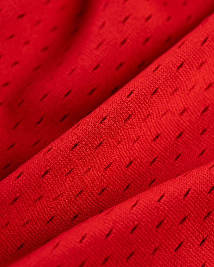 Close-up of the Ebbets Field ELLY DE LA CRUZ BUTTON UP MESH JERSEY in red, featuring small, evenly spaced perforations and visible folds that showcase its textured, breathable mesh fabric design.