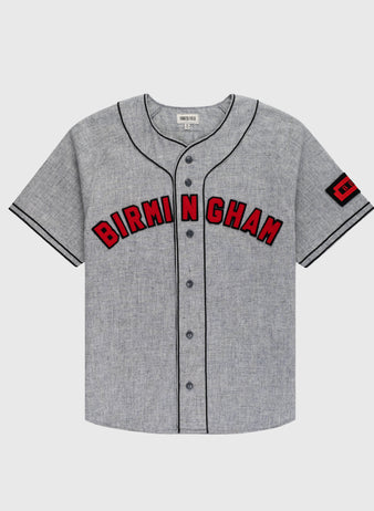 The Ebbets Field Birmingham Black Barons 1948 Authentic Wool Road Jersey is gray with black piping, BIRMINGHAM in bold red/black across the chest, and a red 1921 patch on the left sleeve honoring Negro Leagues Baseball Museum history.