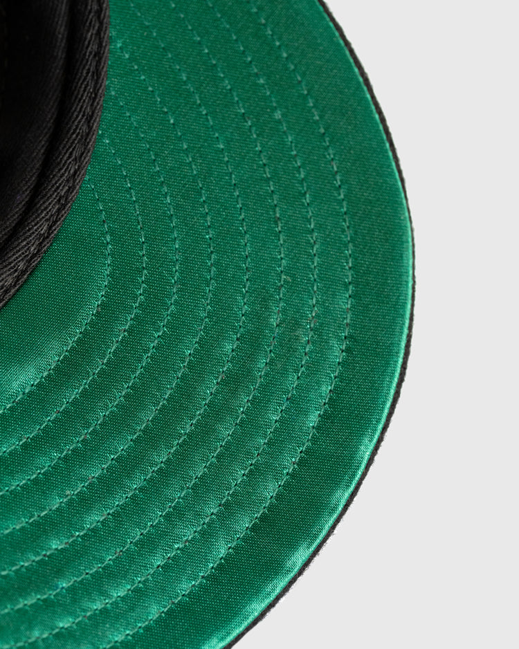 Close-up of the green brim and stitching on the Mossy Oak x Ebbets Field 1945 Kansas City Monarchs Ballcap by Ebbets Field, set against a plain light background. The edge of this classic Negro Leagues hat appears in the upper left corner.