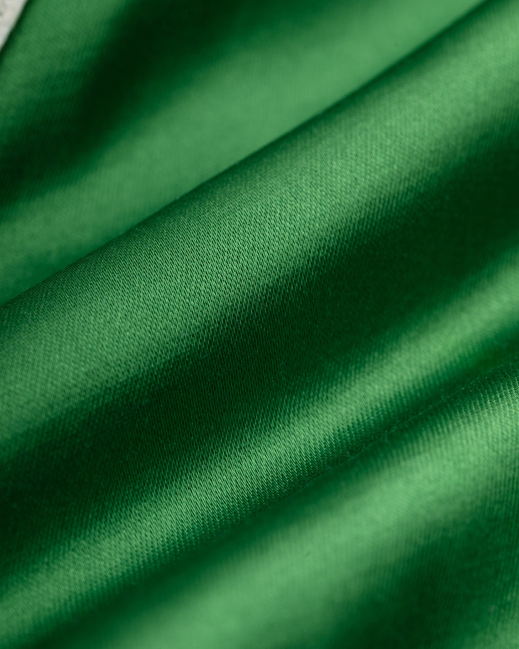 Close-up of smooth, shiny green fabric with gentle folds and soft shadows, highlighting the texture and sheen of the EFF Brooklyn Dodgers 1937 Satin Windbreaker Jacket.