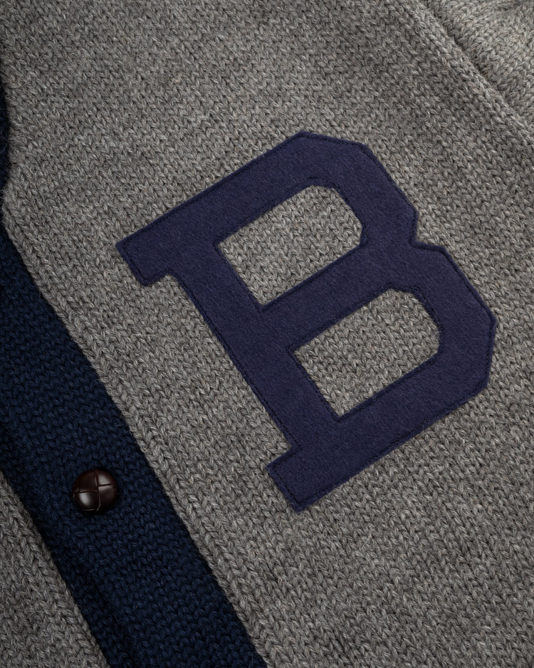 A close-up of the EFF Brooklyn Robins (Dodgers) 1916 wool shawl collar sweater, featuring a gray vintage style with a large dark blue B patch and dark button along navy trim.
