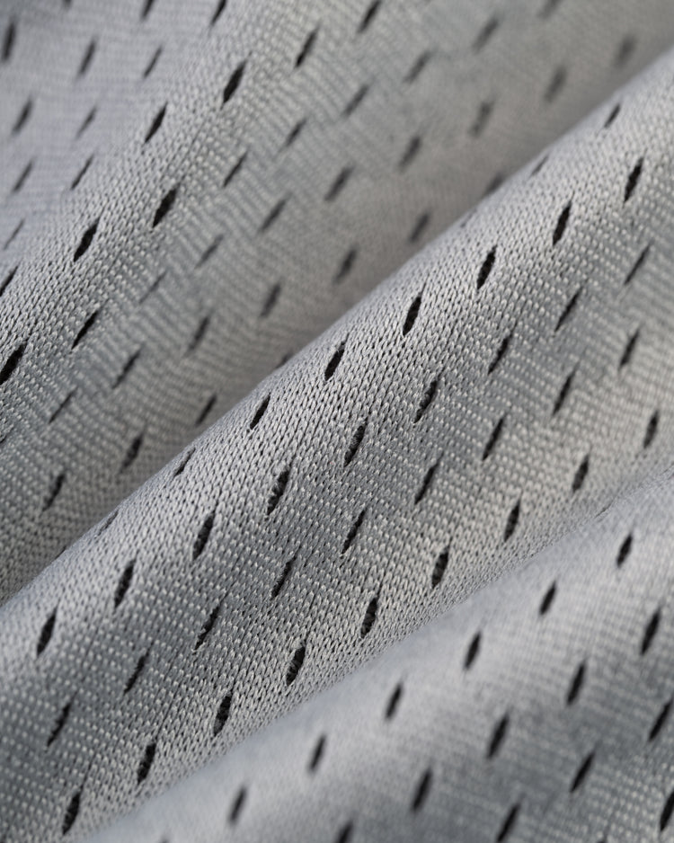 Close-up of the FRANCISCO LINDOR BUTTON UP MESH JERSEY GRY by Ebbets Field, featuring light gray, diamond-shaped perforated fabric for breathability and a soft texture, shown in gentle diagonal folds.