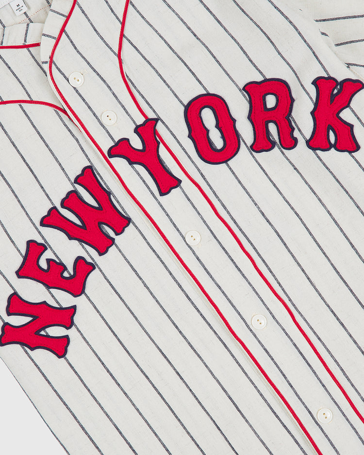 Certainly! Here’s the rewritten sentence using your product data: An authentic 1935 New York Cubans wool road jersey by Ebbets Field, featuring a white, button-up pinstripe design with “NEW YORK” in red letters outlined in navy blue across the chest.
