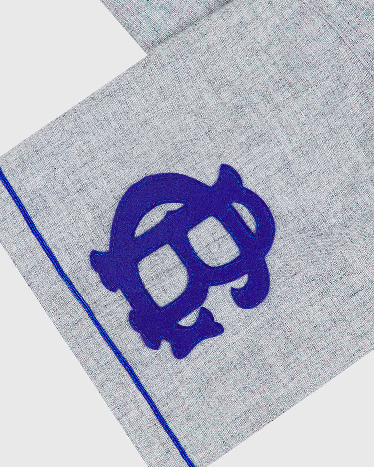A close-up of the Ebbets Field Brooklyn Royal Giants 1915 Authentic Wool Road Jersey fabric in light gray wool, featuring a blue stylized turtle design and a blue seam line running parallel to the edge, reminiscent of the classic style from the original 1915 uniform.