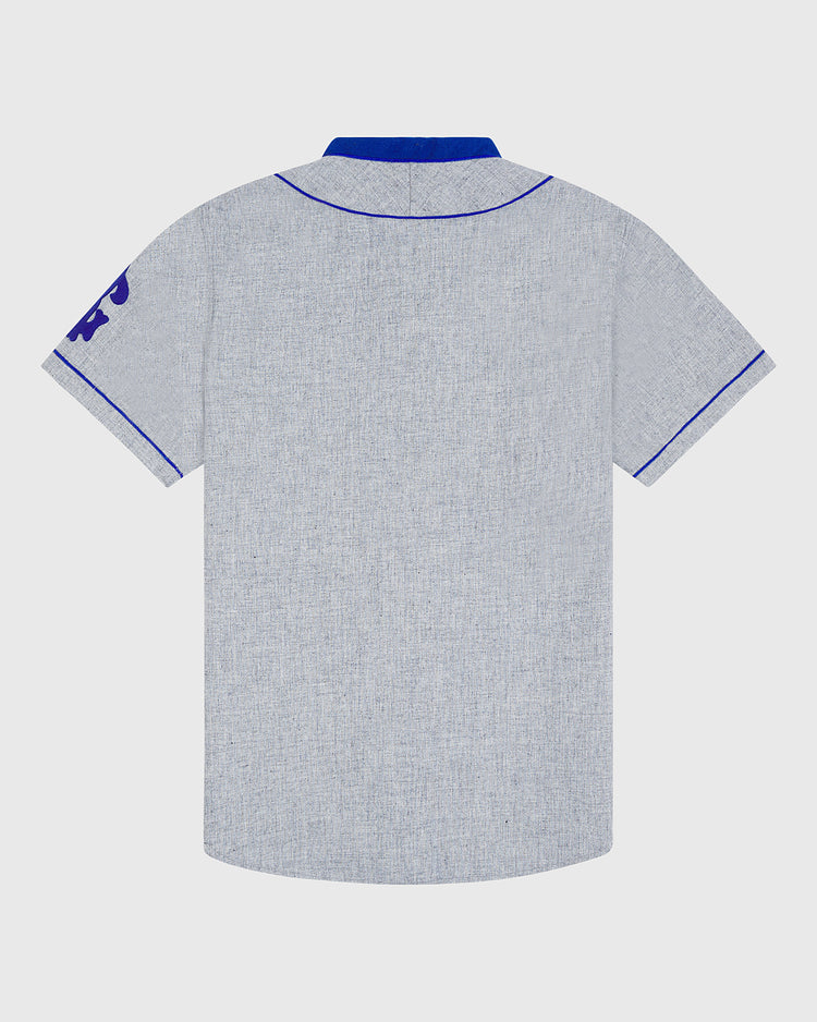 A back view of the Ebbets Field Brooklyn Royal Giants 1915 Authentic Wool Road Jersey is shown in light gray, inspired by the classic Brooklyn Royal Giants design. The short-sleeve shirt features blue stitching along the collar, sleeves, and hem, a blue accent on the inner collar, and a partially visible blue graphic on the left sleeve.