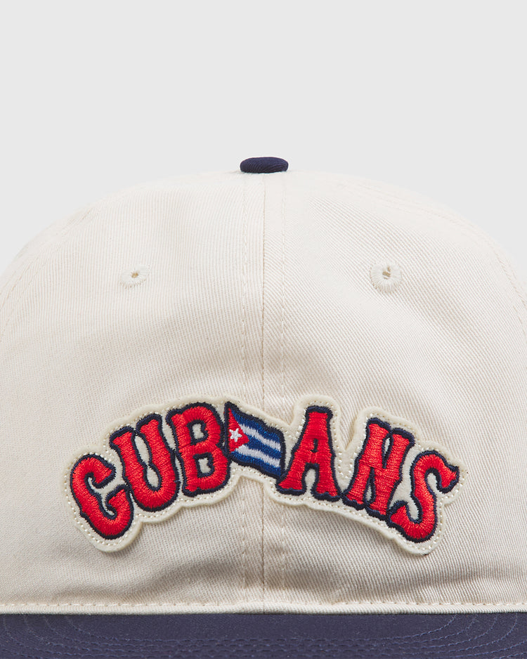 The Ebbets Field New York Cubans Authentic Cotton Ballcap features beige cotton twill with “CUBANS” embroidered in red, where the letter B is replaced by a small Cuban flag. The hat’s brim is dark blue, inspired by the classic style of the original New York Cubans ballcap.