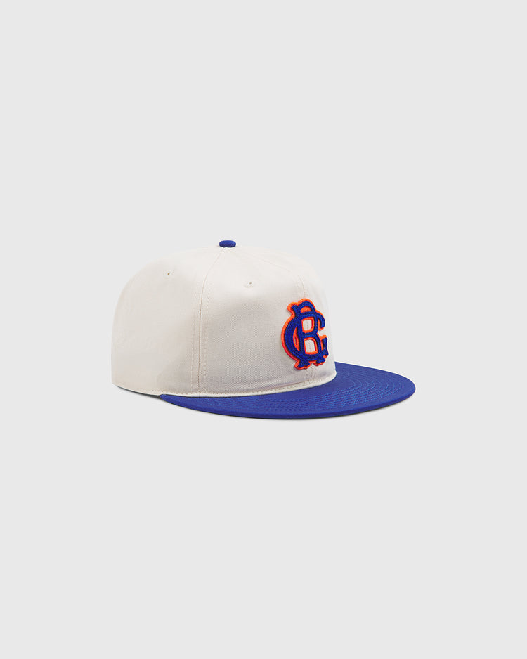 Introducing the Brooklyn Royal Giants Cotton Twill Ballcap by Ebbets Field—a cream cotton twill cap featuring a blue brim and a blue and orange embroidered CB logo on the front, inspired by Black baseball history and displayed against a light gray background.