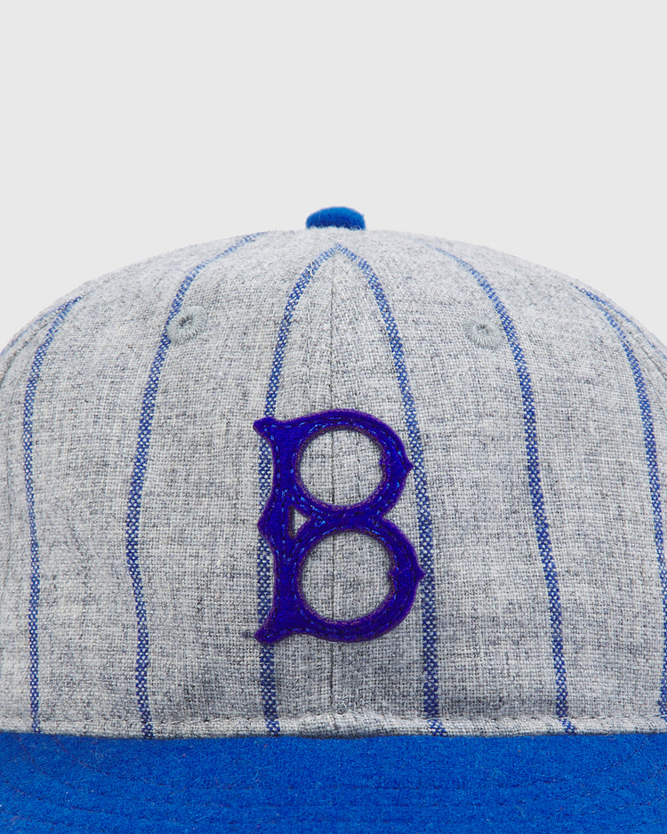 A close-up of the Ebbets Field Brooklyn Royal Giants Authentic Wool Ballcap, featuring gray wool with blue pinstripes and a blue embroidered “B” logo on the front. This cap celebrates Black baseball history with its blue brim and top button, honoring the legacy of the Brooklyn Royal Giants.