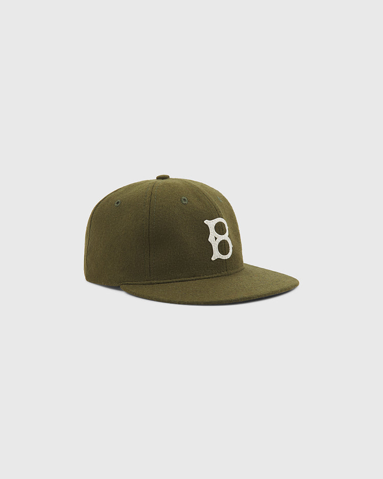 The Ebbets Field Brooklyn Royal Giants Authentic Wool Ballcap features an olive green design with a flat brim and a prominent white embroidered “B” on the front—paying tribute to Black baseball history and the legendary Brooklyn Royal Giants. Photographed against a clean, light gray background, this classic wool cap embodies vintage style and heritage.