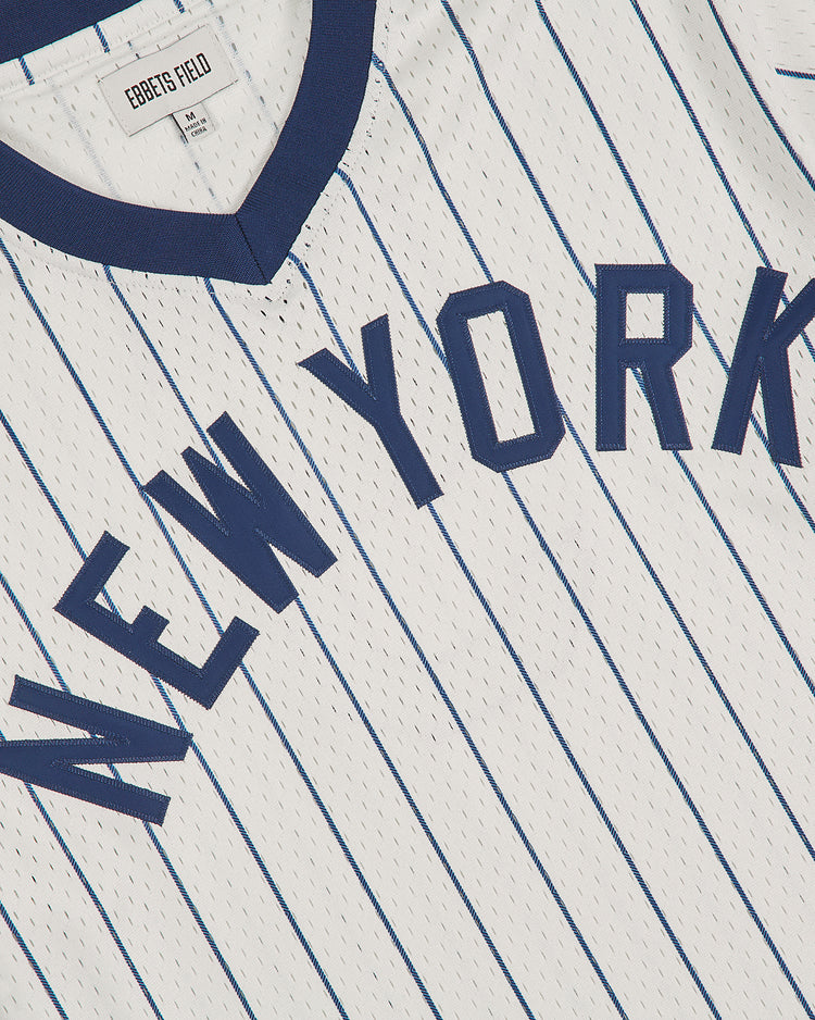A white, pinstriped NY Black Yankees V-Neck Mesh Jersey by Ebbets Field, featuring “NEW YORK” in navy letters across the chest and a navy collar. Inspired by a classic NY Black Yankees jersey, it includes an Ebbets Field label.