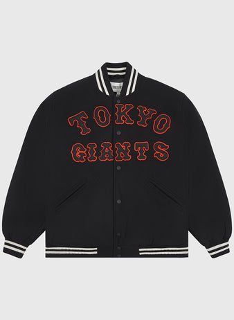 Presenting the Tokyo Giants All-Wool Varsity Jacket by Ebbets Field—a black varsity jacket featuring a white striped collar, cuffs, and hem. “TOKYO GIANTS” is boldly embroidered in large, red outlined letters across the front to honor the legendary Japanese professional baseball team. The jacket includes snap button closures and two front pockets, shown laid flat against a plain background.