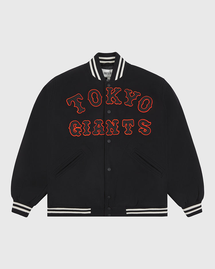 Presenting the Tokyo Giants All-Wool Varsity Jacket by Ebbets Field—a black varsity jacket featuring a white striped collar, cuffs, and hem. “TOKYO GIANTS” is boldly embroidered in large, red outlined letters across the front to honor the legendary Japanese professional baseball team. The jacket includes snap button closures and two front pockets, shown laid flat against a plain background.