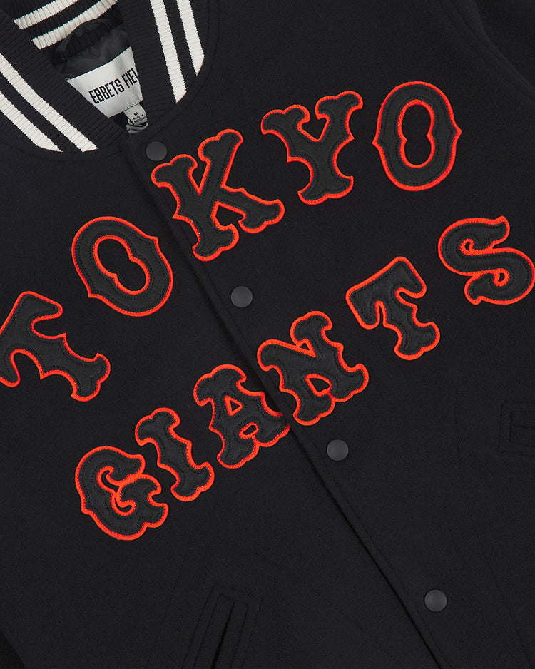 Experience the legacy of Japanese professional baseball with the Tokyo Giants All-Wool Varsity Jacket by Ebbets Field. This classic black jacket features bold, red-outlined “TOKYO GIANTS” lettering across the front, a black collar accented with white stripes, and sleek black snap buttons for a timeless varsity look.